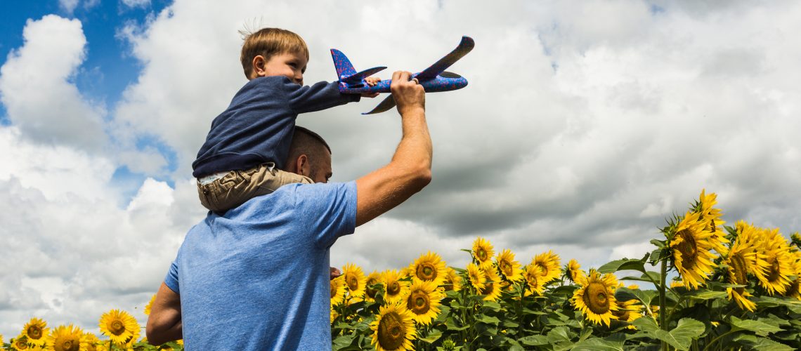 Father and son playing with a toy airplane near the sunflower field